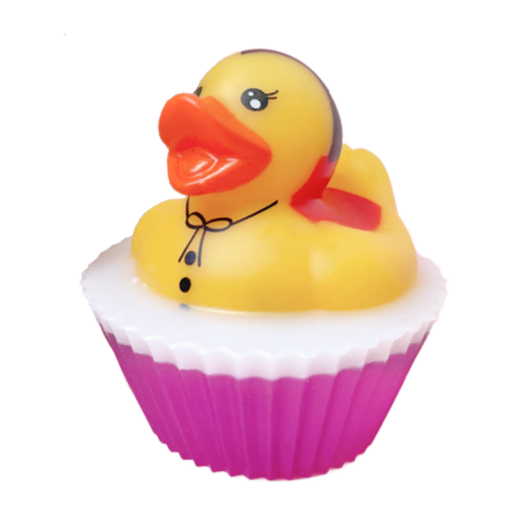 A short cylindrical bright white cupcake shaped block of soap on a bright white cupcake liner that has a bright yellow rubber duck with a bright orange beak, some black eyes, a black bow tie and some black buttons sat on top of it, on a white background.