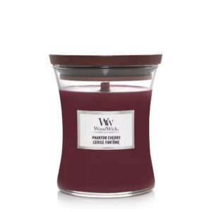 A tall hourglass glass jar full of some dark red wax with a dark wood lid and a bright white label that has WoodWick Candles Phantom Cherry written in bold black writing on it, on a white background.
