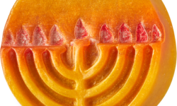 A medium circular bright orange block of soap that has a bright gold Menorah with some bright red flames engraved on it, and some gold lustre all over it, on a white background.