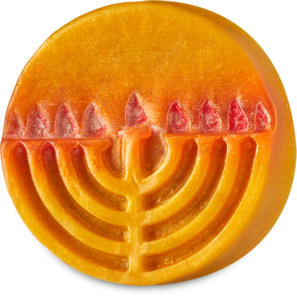 A medium circular bright orange block of soap that has a bright gold Menorah with some bright red flames engraved on it, and some gold lustre all over it, on a white background.
