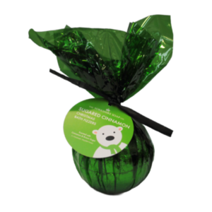 A large spherical shaped bath bomb wrapped in some dark green cellophane and tied with a black ribbon with a dark green label that has The Yorkshire Soap Company Sugared Cinnamon Bath Bomb written in bright white writing and a picture of a White Bear wearing a dark green scarf on it , on a white background.