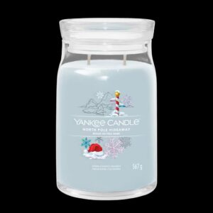 A tall cylindrical glass jar full of some pale blue wax with a label that has Yankee Candle written in bright white writing, North Pole Hideaway written in bright white writing, and a picture of a tall red and white striped north pole, some bright white snowflakes, and some snow covered mountains on it, on a white background.