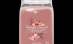 A tall cylindrical glass jar full of some pale pink wax with a label that has Yankee Candle written in bright white writing, Parisian Holiday Brunch written in bright white writing, and a picture of a pile of some golden pancakes covered in some raspberries, a golden brown croissant, and the Eiffel Tower on it, on a white background.
