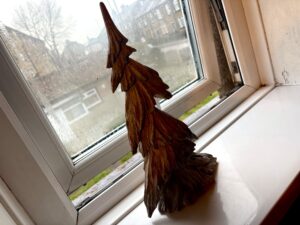 A large triangular bright white and grey resin Christmas Tree on a large rectangular glossy white windowsill infant of a large rectangular foggy glass window.