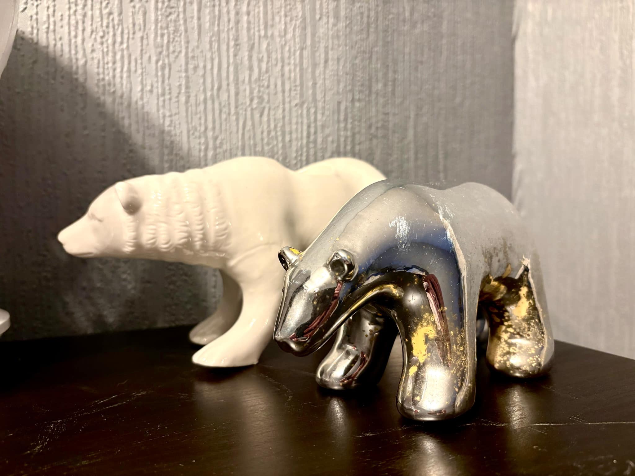A large bright white Polar Bear Tea Light Holder next to a medium sparkly silver Polar Bear ornament, on a black wooden cabinet.