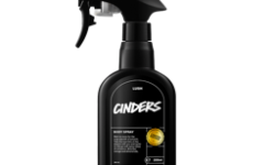 A tall black plastic kitchen spray bottle with a black label that has Lush Cinders Body Spray written in bright white writing on it, on a white background.