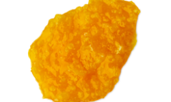 A medium circular puddle of some bright orange shampoo that has some pieces of Course Sea Salt running through it, on a white background.