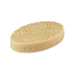 A medium golden yellow oval shaped block of solid massage bar that has a stylised sunburst pattern engraved on it, on a white background.
