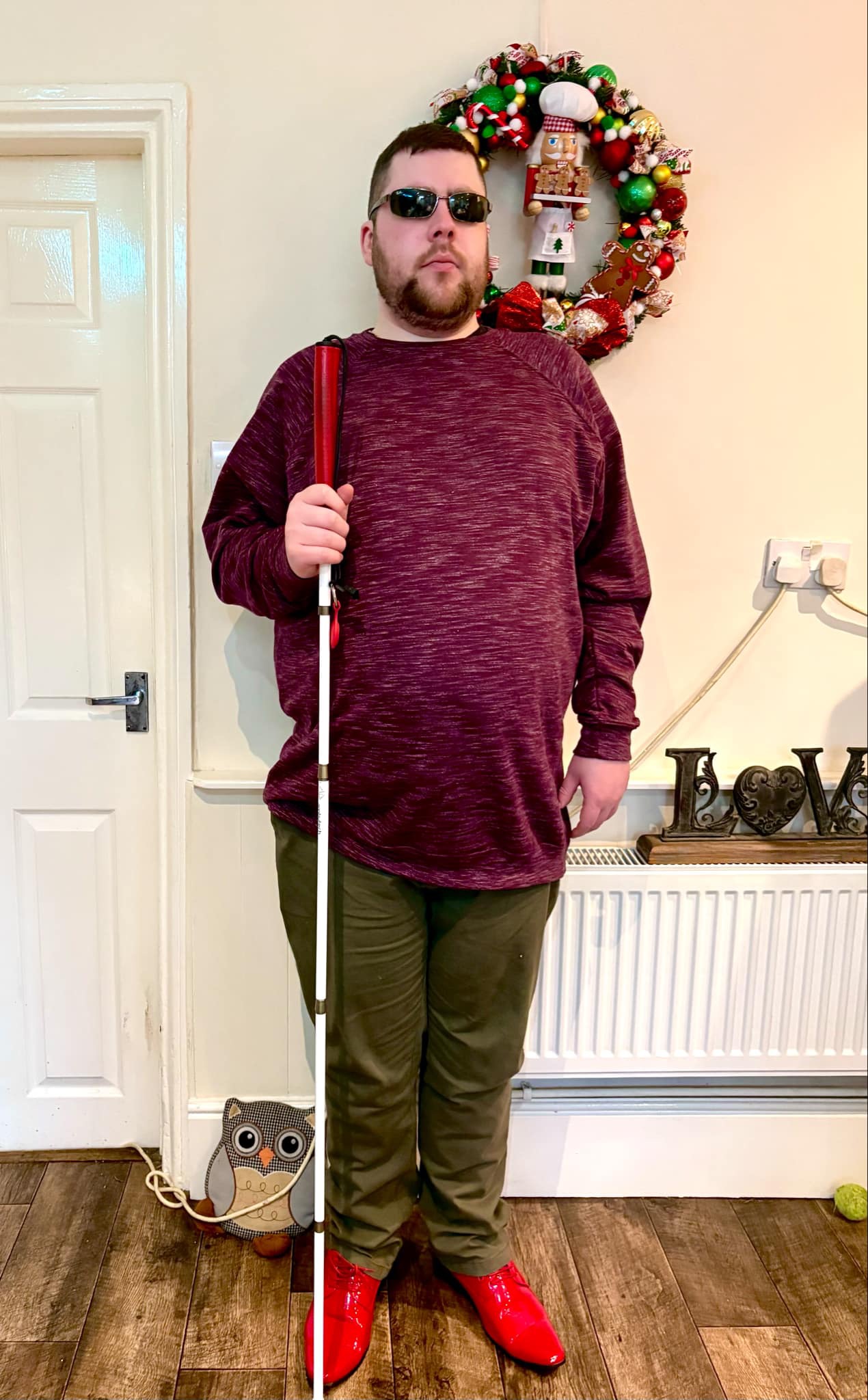 Five Things I Would Like To Achieve In 2026 & Did I Achieve 2025's Goals? A tall bearded man wearing a dark burgundy jumper, a wine red V-Neck t-shirt, a pair of khaki green chino trousers and a pair of shiny red shoes holding a bright white cane with a red leather handle stood against a cream wall.