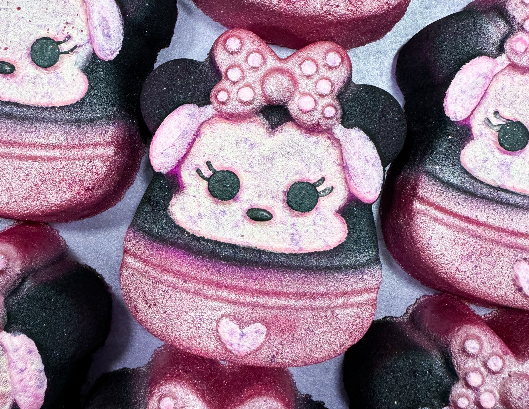 Oh, Minnie. You're All The Music I’ll Ever Need | Tales Of Toria Christmas 2024 Range A pile of some bright white Minnie Mouse Head shaped Bath Bombs that all have a bright pink and white polka dot bow, a small bright pink heart, and a bright white face with some black eyes, a black nose and some bright pink ears on them, on a white background.
