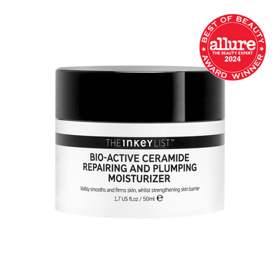 A short cylindrical bright white plastic tub with a black plastic lid and a bright white label that has The INKEY List Bio-Active Repairing & Plumping Ceramide Moisturiser written in bold black writing and a picture of a black stripe on it, on a white background.