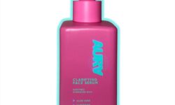 A tall rectangular bright pink glass bottle with a bright pink rubber pipette lid that has Aura Clarifying Face Serum written in bright turquoise writing on it, on a white background.