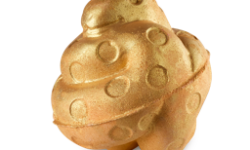 A medium bright caramel rounded hexagonal shaped bath bomb that has a coiled up snake with some bright gold spots all over it on top of it and is covered in some bright gold lustre, on a white background.