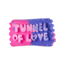 A medium gradient bright pink and purple ticket stub shaped bath bomb that has Tunnel Of Love written in bright white writing and a picture of a love heart engraved on it, on a white background.
