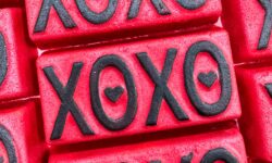 A pile of some large bright red rectangular shaped bath bombs that all have XO and XO written in bold black writing and a black love heart engraved on them, on a white background.