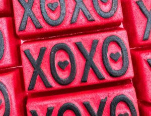 A pile of some large bright red rectangular shaped bath bombs that all have XO and XO written in bold black writing and a black love heart engraved on them, on a white background.