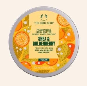 A short cylindrical dark green plastic tub with a golden yellow lid and a golden yellow label that has The Body Shop Shea & Goldenverry Body Butter written in dark green writing and some pictures of some bright orange and yellow golden berries and leaves on it, on a white background.