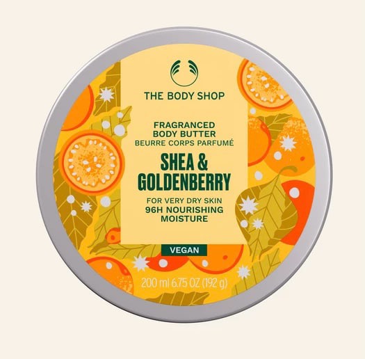Following A Golden Star To A Moisturised Christmas | The Body Shop Christmas 2024 Range A short cylindrical dark green plastic tub with a golden yellow lid and a golden yellow label that has The Body Shop Shea & Goldenverry Body Butter written in dark green writing and some pictures of some bright orange and yellow golden berries and leaves on it, on a white background.