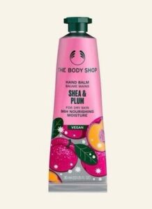 A long and thin conical metallic bright pink tube with a metallic dark green lid and a bright pink label that has The Body Shop Shea & Plum Hand Balm written in dark green writing and some pictures of some bright purple plums on it, on a white background.