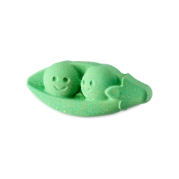 A small bright pea green pea pod shaped bath bomb that has two dark green peas inside it with some smiling faces engraved on them, on a white background.
