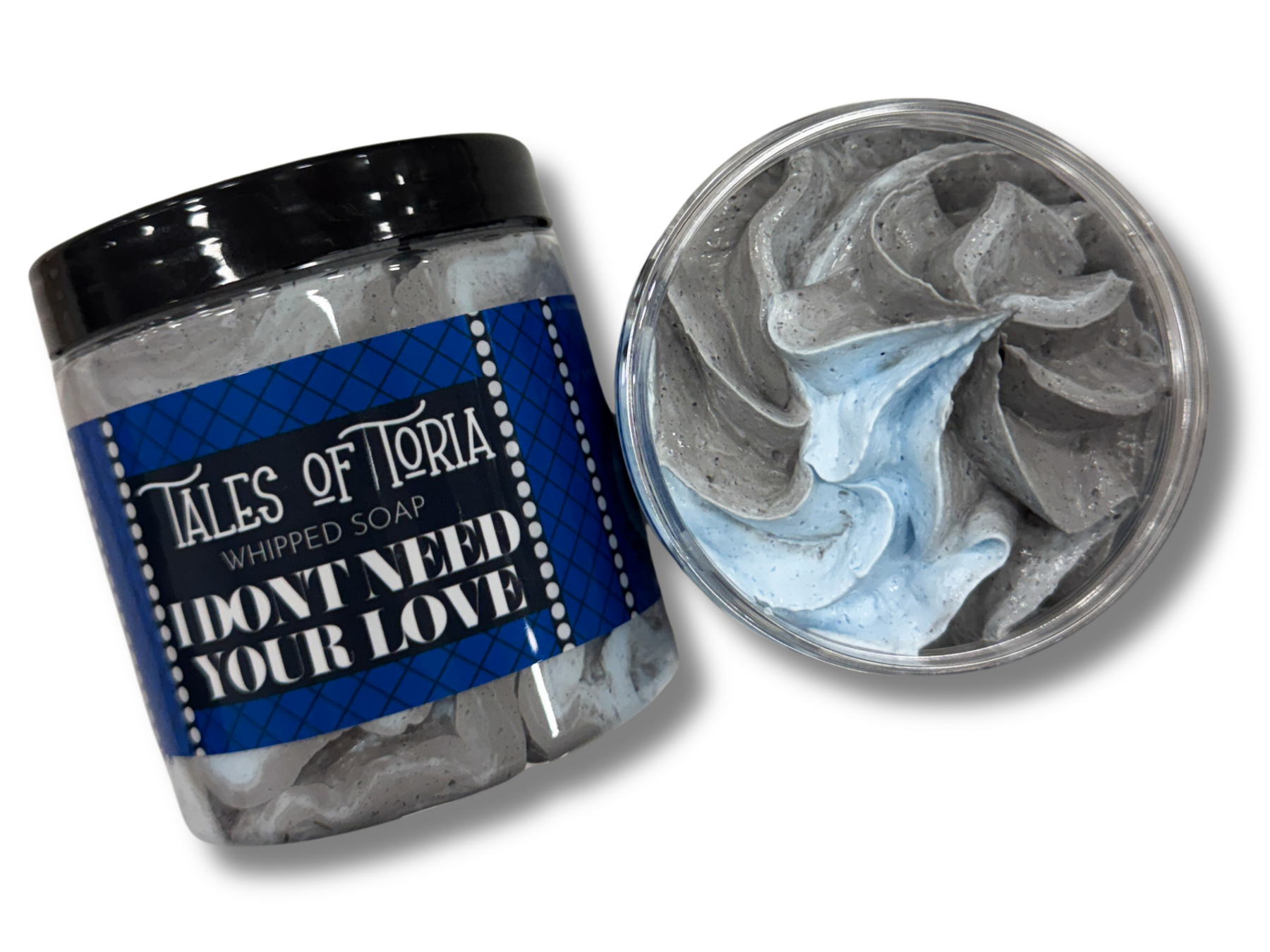 A tall cylindrical clear plastic tub full of some gradient bright grey and light blue whipped soap with a black plastic lid and a light blue label that has Tales of Toria I Don’t Need Your Love Whipped Soap written in bright white writing and some pictures of some light blue diamonds on it, on a white background.