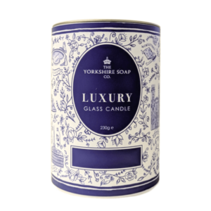 A tall bright white cardboard tube that has The Yorkshire Soap Company Afternoon Tea Glass Candle written in bright white writing inside a dark blue oval, a picture of a black crown, and some pictures of some bright white leaves on it, on a white background.