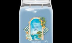 A tall cylindrical glass jar full of some pale blue wax with a label that has Yankee Candle written in bright white writing, Azure Sky written in bright white writing, and a picture of a Sailboat bobbing around on the Water on it, on a white background.
