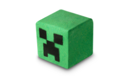 A medium bright green cube shaped bath bomb that has some black square eyes and a frowning mouth engraved on it, on a white background.