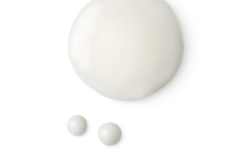 A medium circular puddle of some translucent creamy white conditioning spray, on a white background.