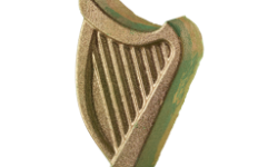 A medium bright green harp shaped bath bomb that has a yellow outline and is covered in some gold lustre, on a white background.
