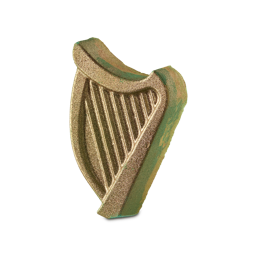 Boy, Give Your Tab Some Closure. Ain’t Your Four-Leaf Clover | Lush St. Patrick's Day 2025 Range A medium bright green harp shaped bath bomb that has a yellow outline and is covered in some gold lustre, on a white background.