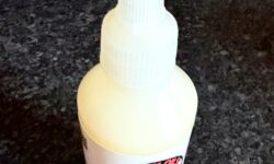 A short cylindrical clear plastic bottle full of some creamy white liquid with a bright white plastic lid and a bright white label that has Thirty 1 Oils Sherbet Zombie Beard Hybrid written in bold black writing and a picture of a man’s face with a blue beard on it, on a white background.