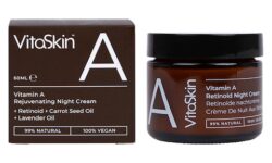 A short cylindrical dark brown glass jar with a metallic black lid and a dark brown label that has Vitaskin Rejuvenating Night Cream written in bold bright white writing and a picture of a letter A on it next to a short square dark brown cardboard box that has Vitaskin Rejuvenating Vitamin A Night Cream written in bright white writing on it, on a white background.
