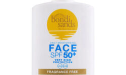 A short rectangular white plastic bottle with a white plastic lid that has Bondi Sands SPF50+ Fragrance Free Face Sunscreen Fluid written in dark blue writing, a picture of a bright yellow circle, and a picture of a bright gold stripe on it, on a white background.