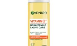 A tall cylindrical bright yellow plastic bottle with a bright white plastic lid and a bright white label that has Garnier Vitamin C* Brightening Liquid Care written in bold black writing on it, on a white background.