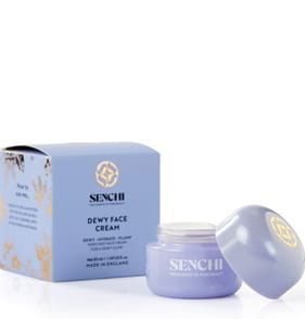 A short cylindrical light purple glass jar with a light purple plastic lid that has Senchi Dewy Face Cream written in bright white writing on it next to a short square light purple cardboard box that has Senchi Dewy Face Cream written in bright white writing on it, on a white background.