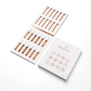 Ten small cylindrical clear glass Vials full of some amber coloured liquid with white labels that has Abu Dhabi, Accra, Berlin, Brooklyn,Buenos Aires, Istanbul, London, Los Angeles, Naples, and Tokyo written in bold black writing on them inside a large rectangular bright white cardboard box, on a white background.