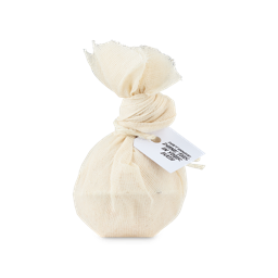 A small bright white spherical shaped bath bomb wrapped in a piece of creamy white Muslin cloth that’s tied in a knot with some bright white string with a bright white label that has Don’t Unwrap, dunk this in your bath written in bold black writing on it, on a white background.