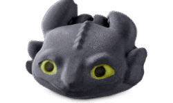 A large black dragon’s head shaped bath bomb that has some large bright green eyes, some black slicked-back ears, and a wide toothless mouth engraved on it, on a white background.