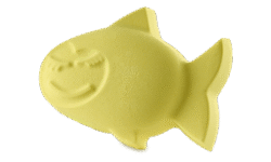 A small bright yellow fish shaped bath bomb that has a wide smile and some closed eyes with some eyelashes engraved on it, on a white background.