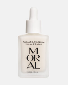 A short square bright white glass bottle with a bright white rubber pipette lid and a bright white label that has Moral Radiant Blend Serum written in bold black writing on it, on a white background.