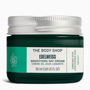 A short cylindrical dark green glass jar with a silver metallic lid that has The Body Shop Edelweiss Smoothing Day Cream written in dark green writing on it, on a white background.