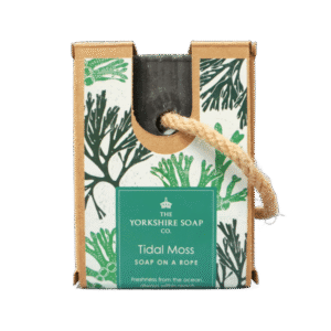 A medium rectangular dark blue block of soap inside a medium rectangular cardboard box with a dark green label that has The Yorkshire Soap Company Tidal Moss Soap On A Rope Bar written in bold bright white writing, some pictures of some bright green pieces of Seaweed, and a piece of light brown rope tied around it, on a white background.