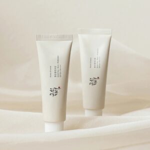 A tall conical creamy white plastic tube with a creamy white plastic lid that has Beauty of Joseon Relief Sun Rice + Probiotic SPF50+ PA++++ written in bold black writing on it next to a tall conical creamy white plastic tube with a creamy white plastic lid that has Beauty of Joseon Relief Sun Rice + Probiotic SPF50+ PA++++ written in bold black writing on it, on a white background.
