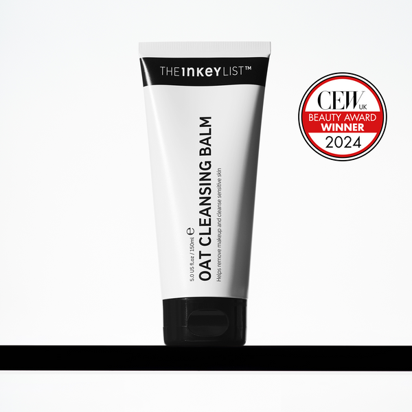 Tattooing The Soothing Power Of Oats Into My Skin | The INKEY List Oat Cleansing Balm A tall conical bright white plastic tube with a black plastic lid that has The INKEY List Oat Cleansing Balm written in bold black writing on it, on a white background.