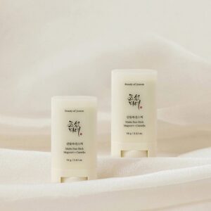 A short rounded rectangular creamy white plastic tube with a circular twist up mechanism at the bottom of it that has Beauty of Joseon Mugwort + Camilia Matte Sun Stick SPF50+ PA++++ written in bold black writing on it next to a short rounded rectangular creamy white plastic tube with a circular twist up mechanism at the bottom of it that has Beauty of Joseon Mugwort + Camilia Matte Sun Stick SPF50+ PA++++ written in bold black writing on it, on a creamy white background.