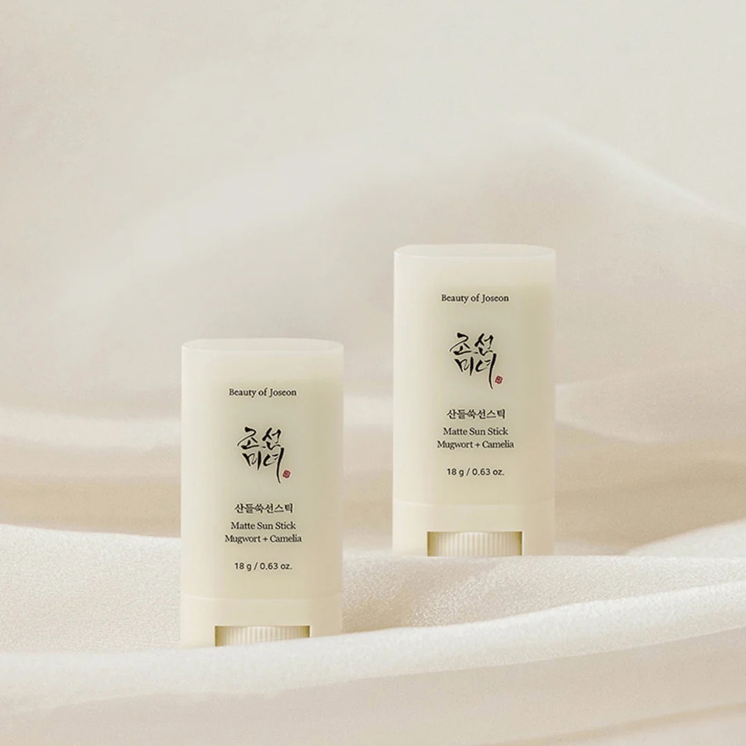 The Beauty Of Convenient Suncare | Beauty Of Joseon Mugwort + Camilia Matte Sun Stick SPF50+ PA++++ A short rounded rectangular creamy white plastic tube with a circular twist up mechanism at the bottom of it that has Beauty of Joseon Mugwort + Camilia Matte Sun Stick SPF50+ PA++++ written in bold black writing on it next to a short rounded rectangular creamy white plastic tube with a circular twist up mechanism at the bottom of it that has Beauty of Joseon Mugwort + Camilia Matte Sun Stick SPF50+ PA++++ written in bold black writing on it, on a creamy white background.