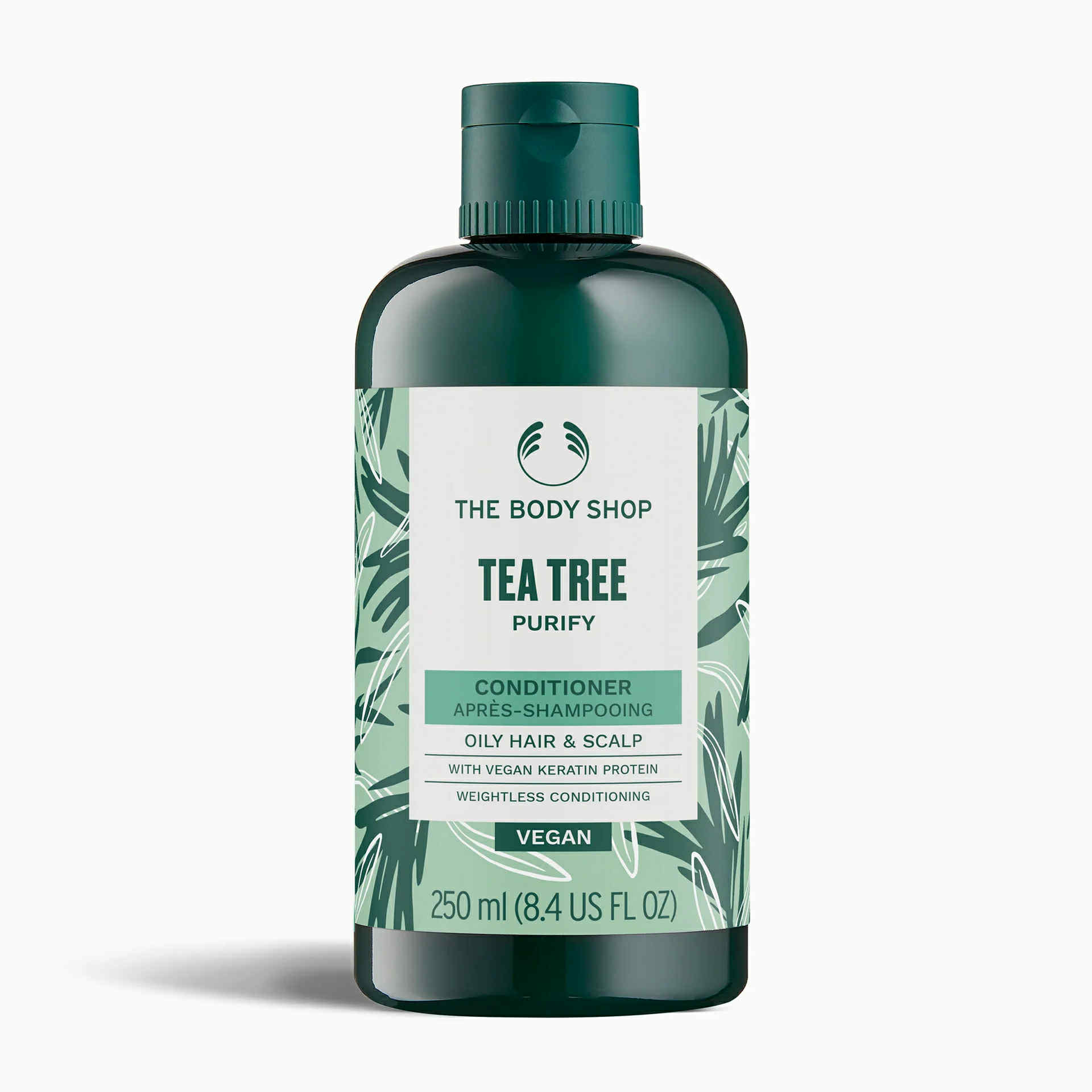 A short cylindrical dark green plastic bottle with a dark green plastic lid and a bright green label that has The Body Shop Tea Tree Purifying & Balancing Conditioner written in dark green writing and some pictures of some dark green tea tree leaves on it, on a white background.