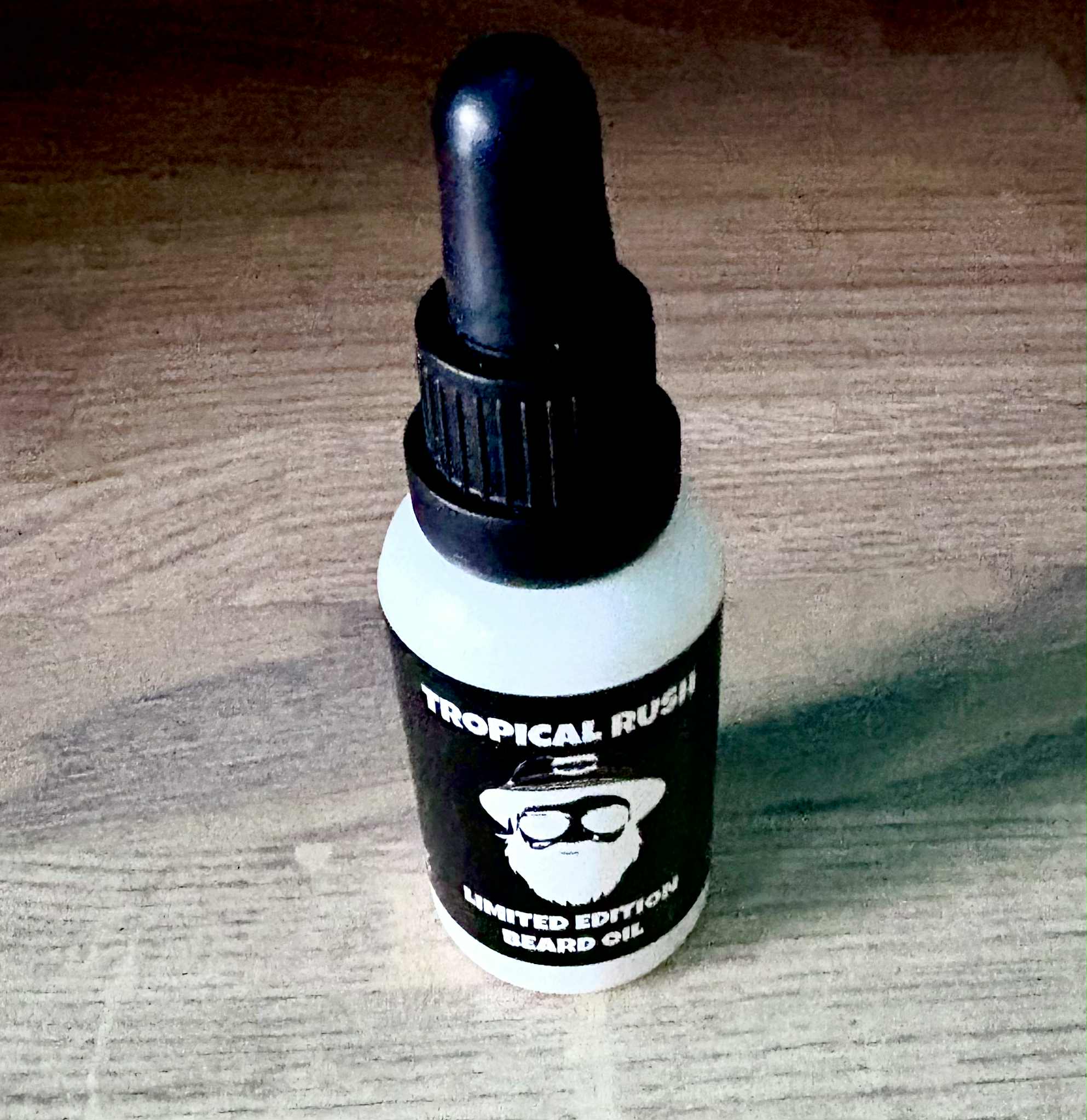 In The Rush To Get To The Airport, I Think I Forgot My Beard Oil | Thirty 1 Oils Tropical Rush Beard Oil A short cylindrical brown glass bottle with a black rubber pipette lid and a white label that has Thirty 1 Oils Tropical Rush Beard Oil written in bold black writing and a picture of a man wearing a pair of sunglasses on it, on a white background.
