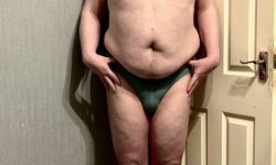 A tall bearded man with his hands on his hips wearing a pair of dark green briefs with a dark green waistband that has Box Menswear written in bold black writing on it stood against a white wooden door.